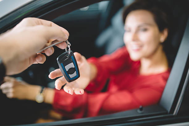 Young woman sitting in new car and taking the keys from the car dealer